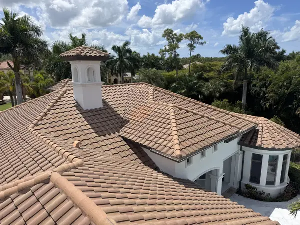A high-angle view across a tiled roof of a multi-story home surrounded by trees.