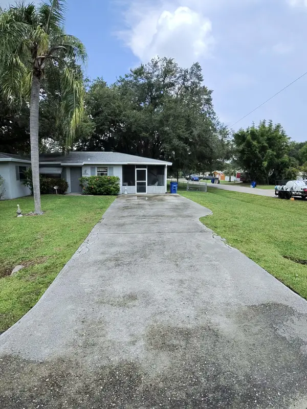 A long concrete driveway leading to a house with a screen enclosure and a palm tree.