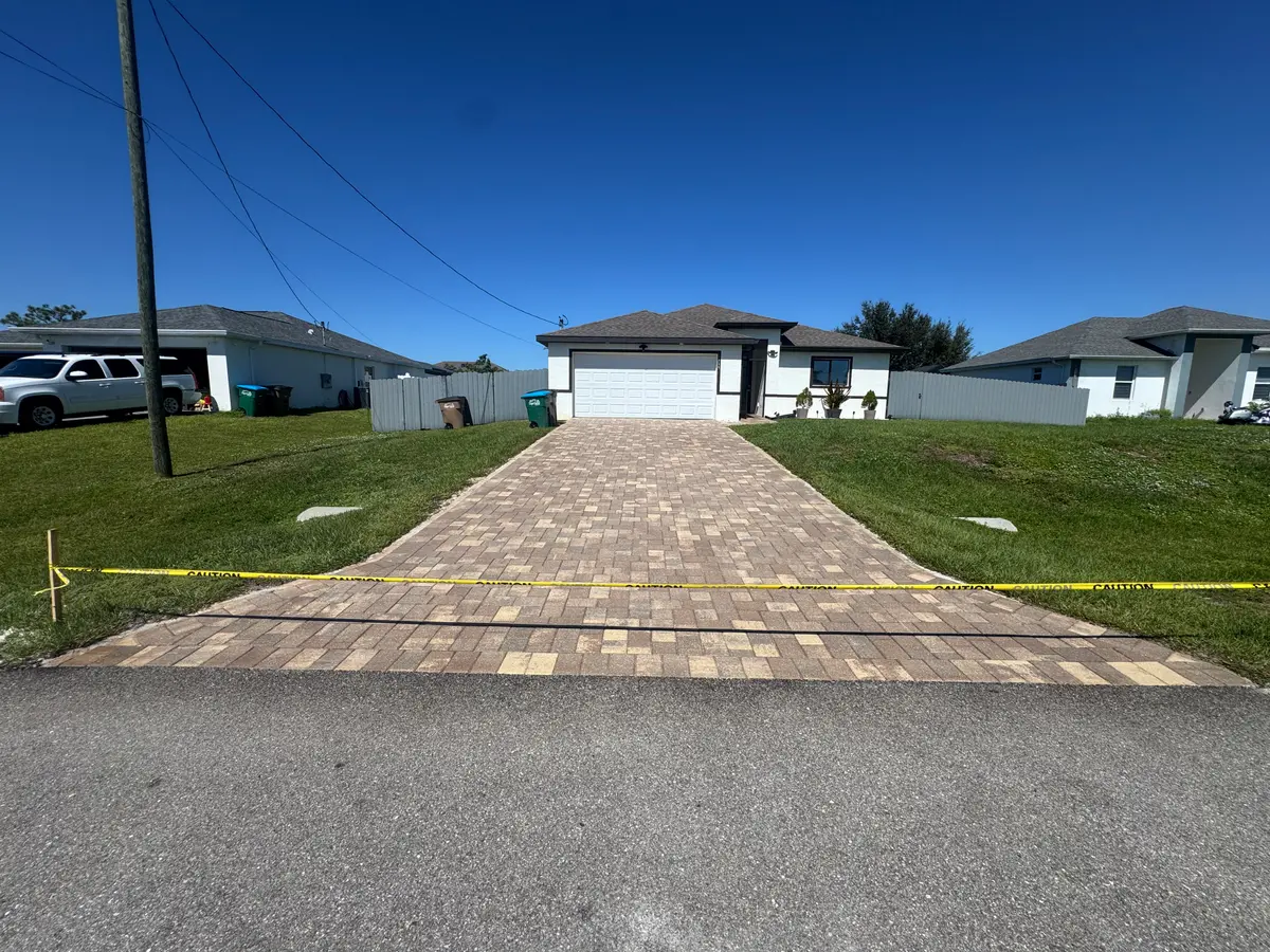 A driveway of light-coloured pavers taped off in front of a house.