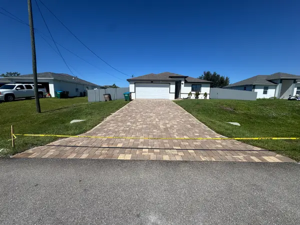 A driveway of light-coloured pavers taped off in front of a house.