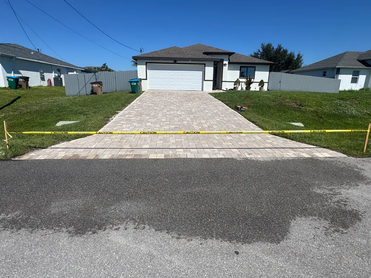 A driveway of light-coloured pavers with caution tape strung across the front.