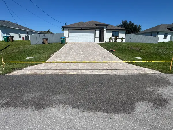 A driveway of light-coloured pavers with caution tape strung across the front.