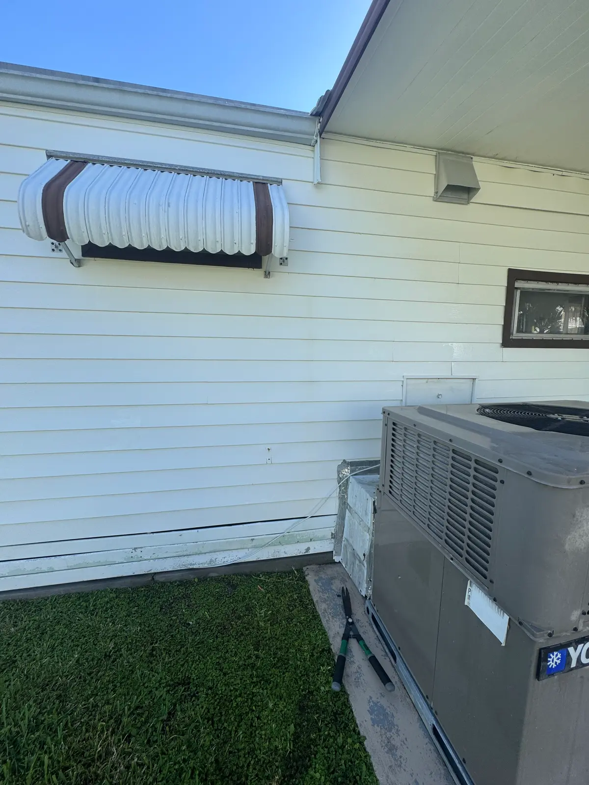 A cleaned side wall of light siding with an HVAC unit and a window awning.