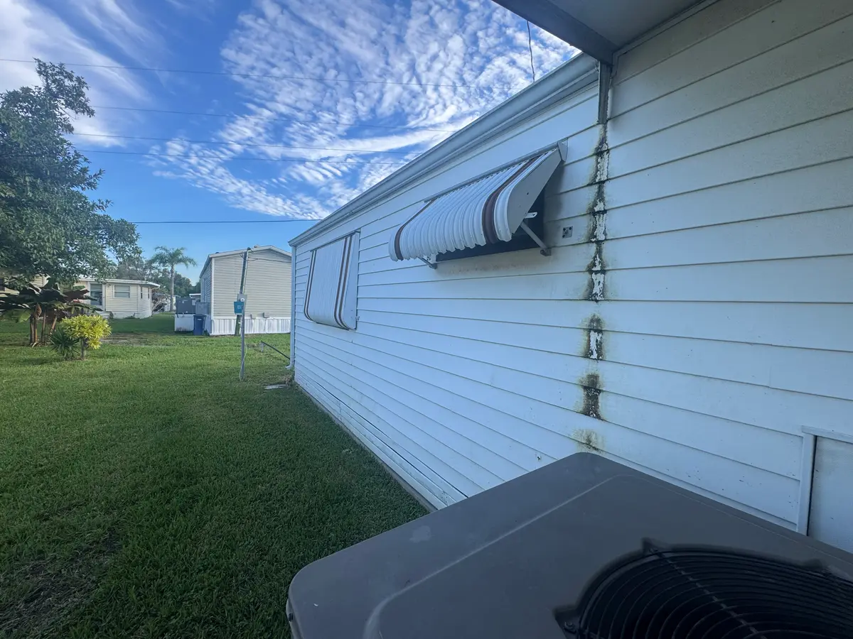 A side wall of white siding with grime streaks, an HVAC unit and metal awnings.