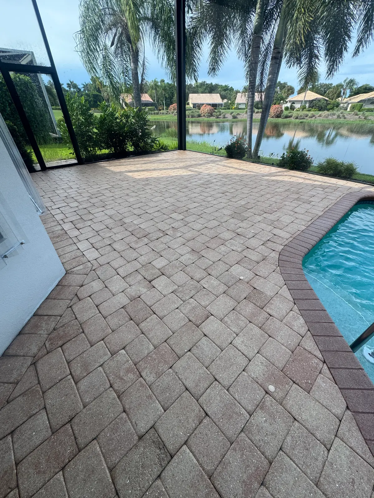 A paver pool deck beside a swimming pool with a lake beyond.