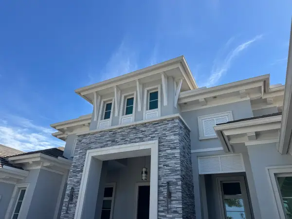 The front of a multi-story home with grey walls and stone accents under a blue sky.