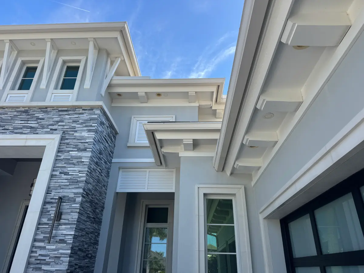 The wall and roof eaves of a light grey house seen from below.