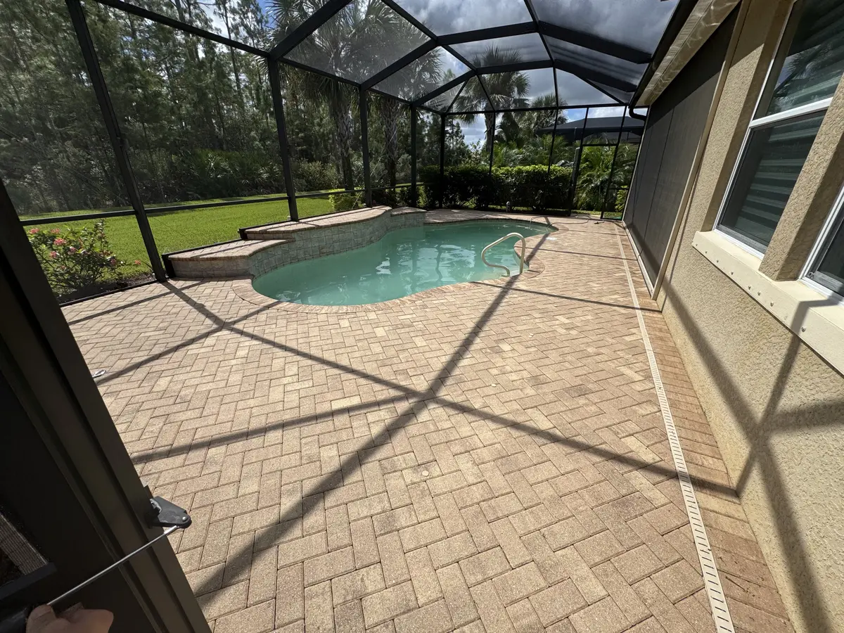 A cleaned brick paver pool deck inside a screen enclosure.