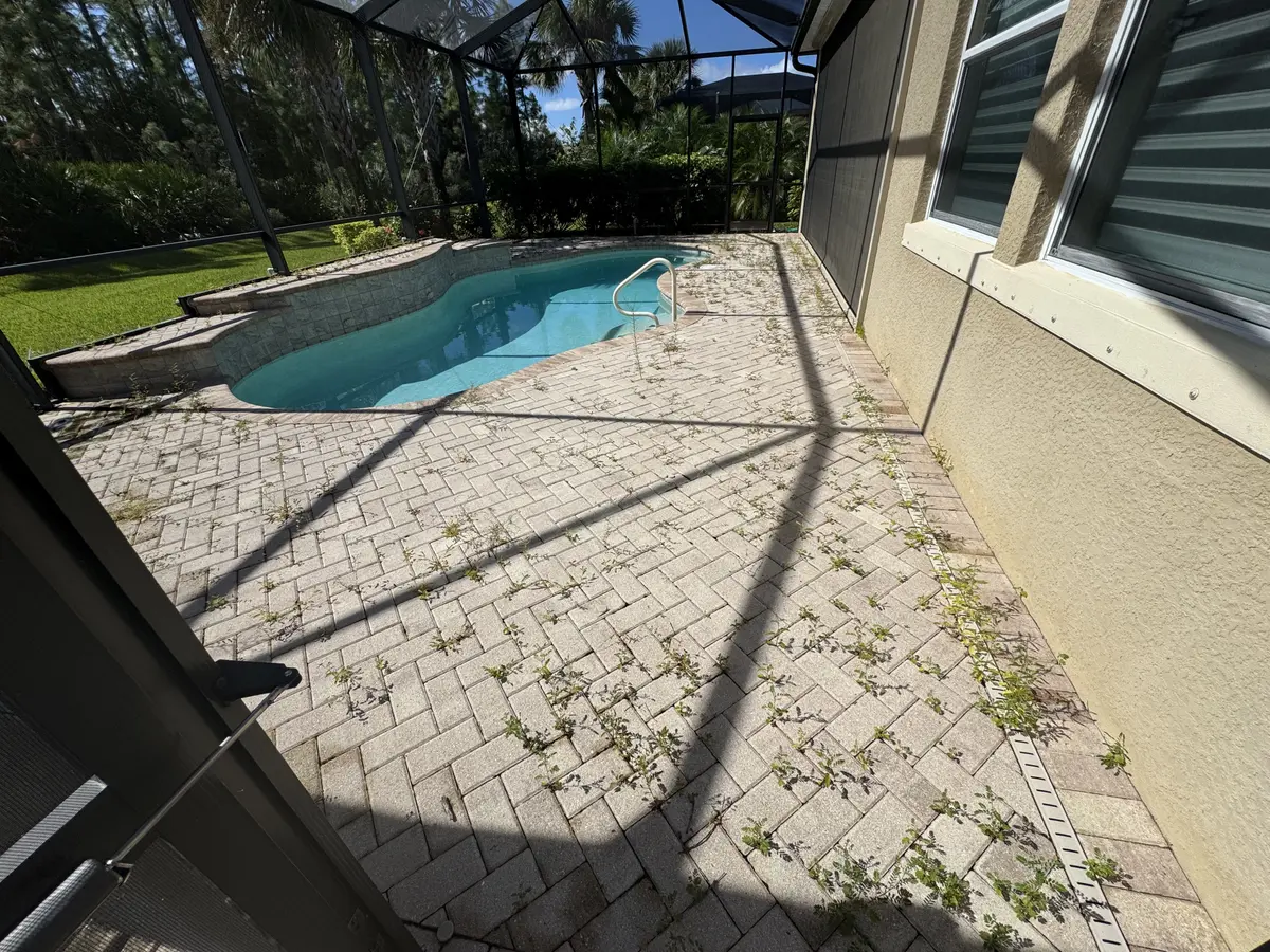 A brick paver pool deck with weeds growing between the pavers inside a screen enclosure.
