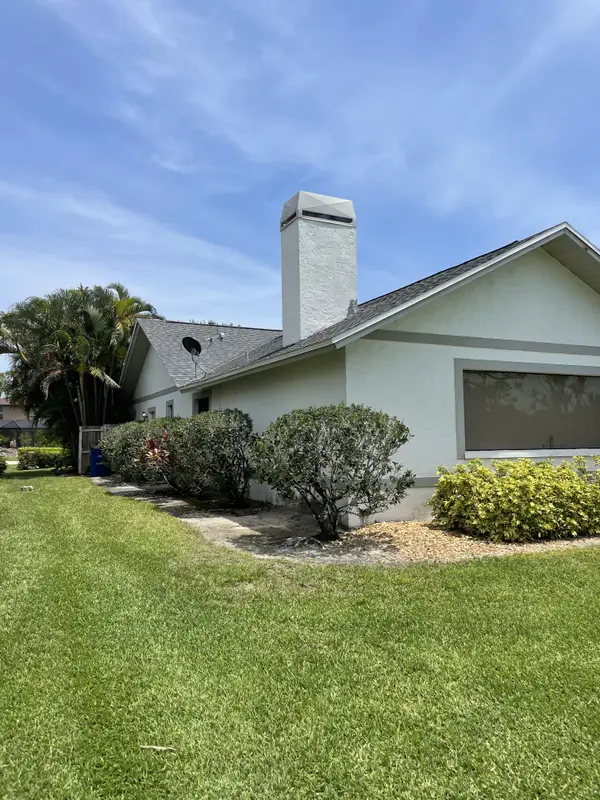 The side wall and chimney of a house behind trimmed shrubs.