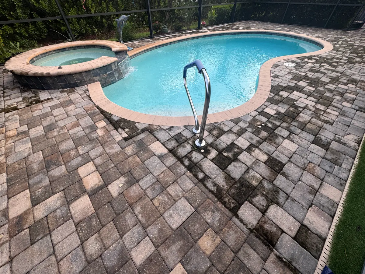 A paver pool deck with dark organic growth across part of the surface.