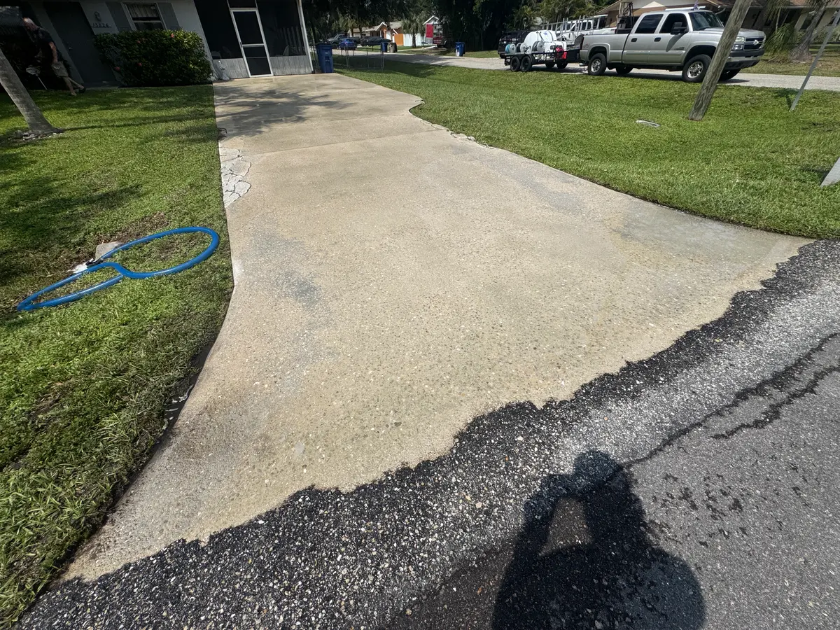 A concrete driveway running from a home toward the street with a truck parked nearby.